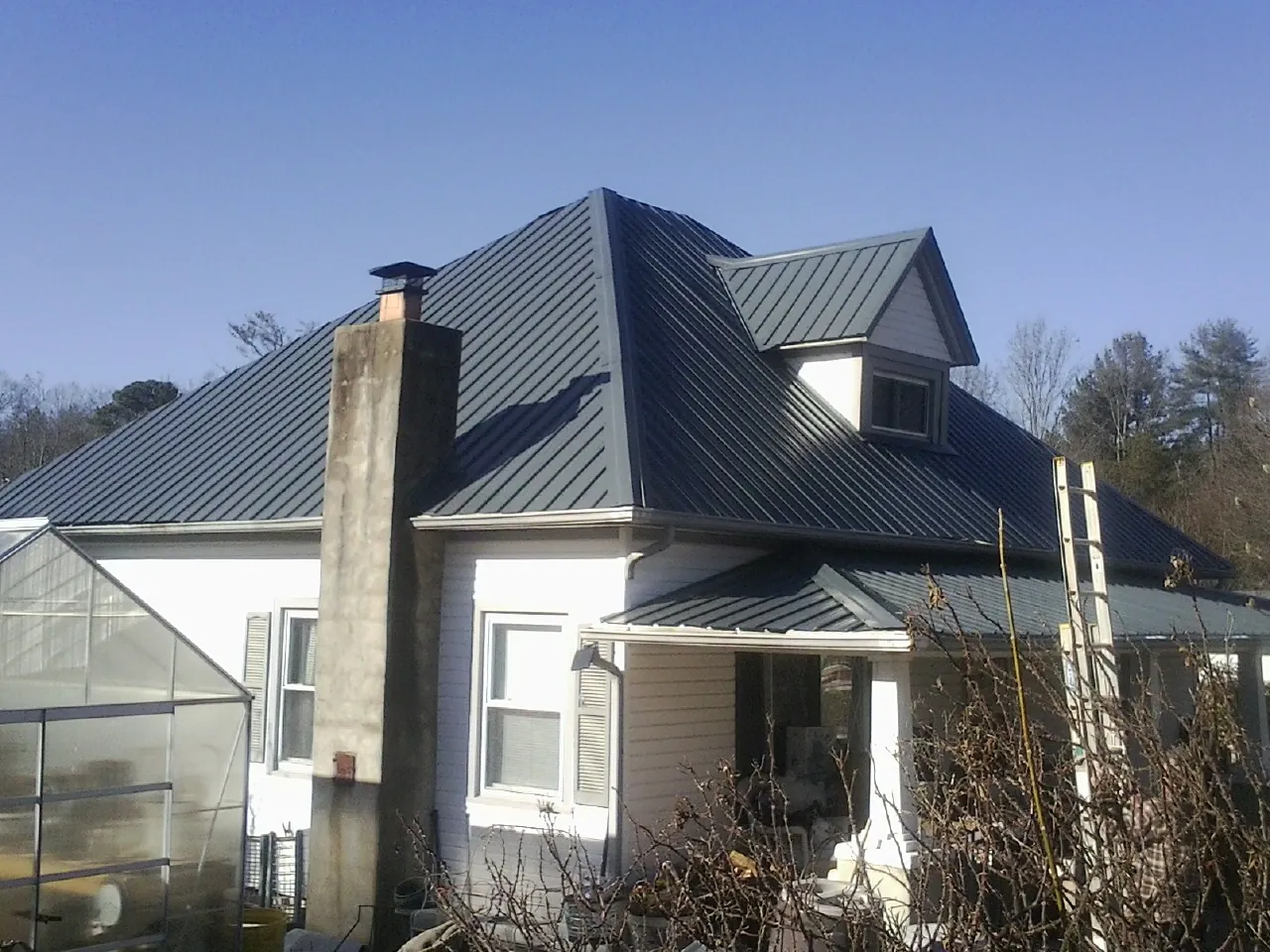Dark blue standing seam metal roof on a white farmhouse with dormer — Slate & Tile Roof Repair by Roofing Brothers in Kerkhoven