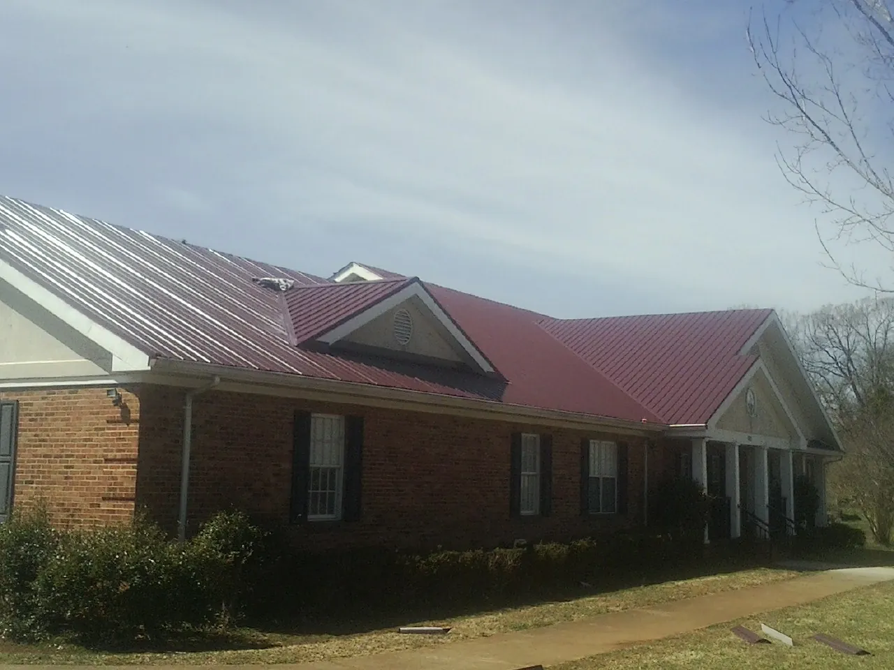 Red metal roof with gabled entries on a long brick building, from a Hail Damage Roof Repair job in Kerkhoven