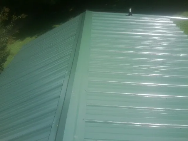 New green metal panels meeting at the ridge of a roof — Flat Roof Repair work by our crew in Kerkhoven