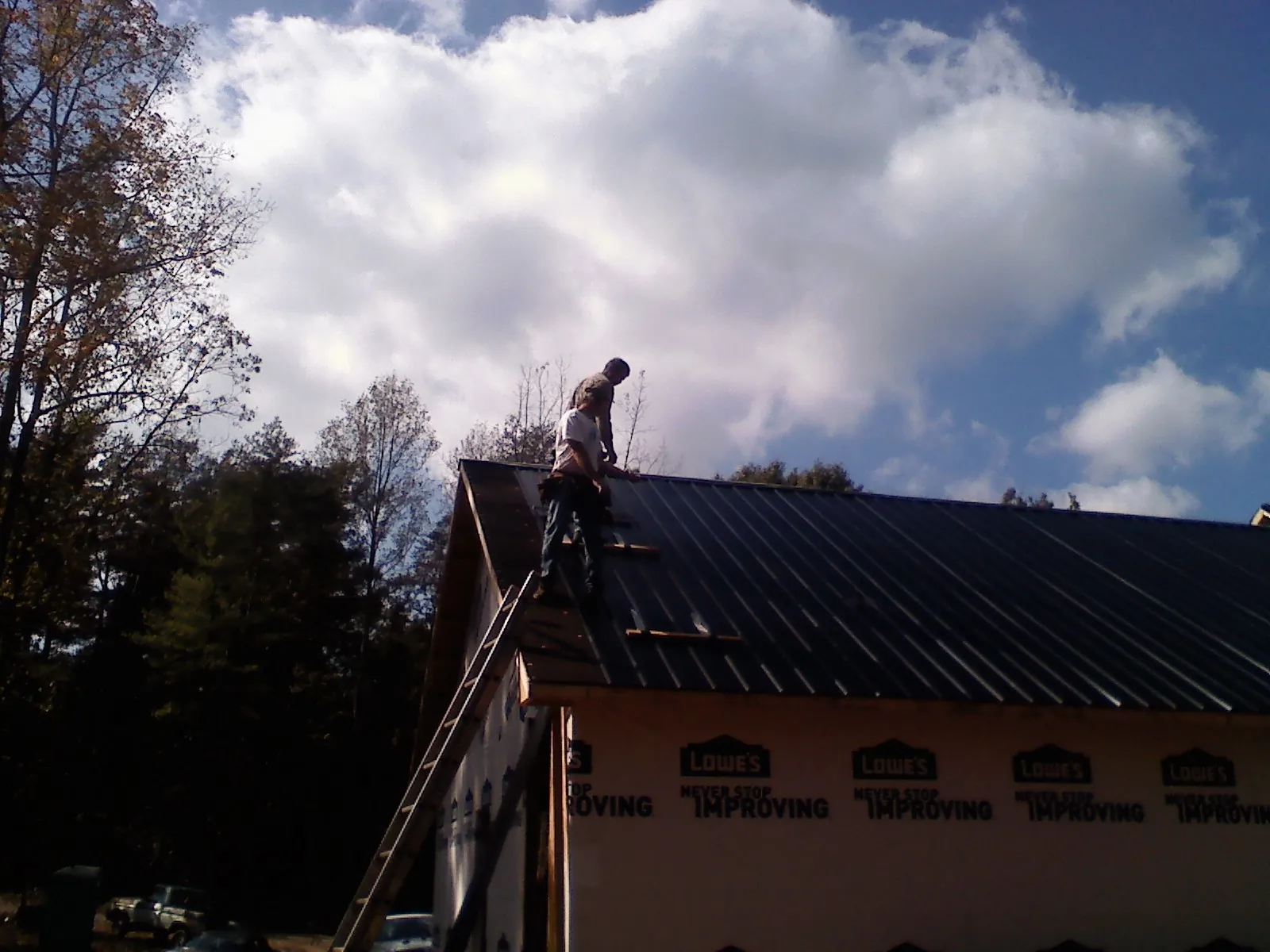 Roofer fastening dark metal panels high against a cloudy sky, from a Roof Inspection job in Kerkhoven