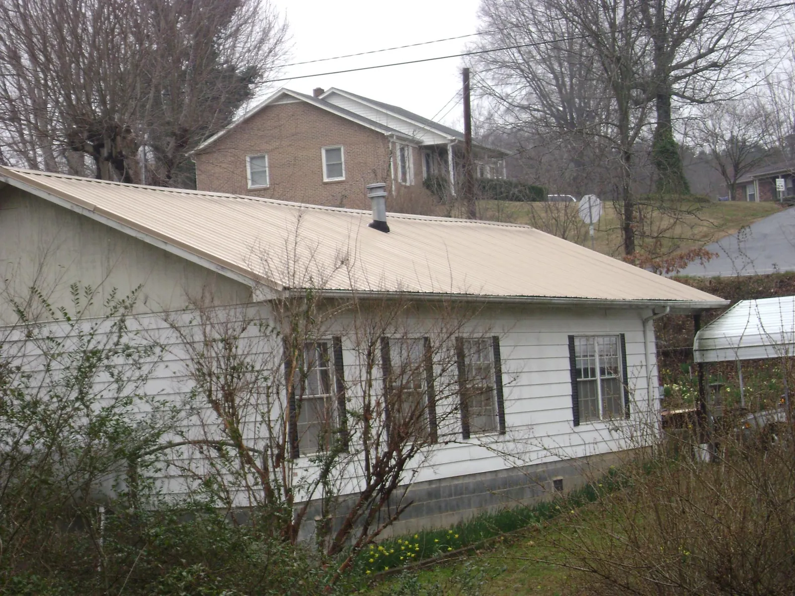 Tan metal roof on a white sided house set into a hillside — Commercial Roofing by Roofing Brothers in Kerkhoven