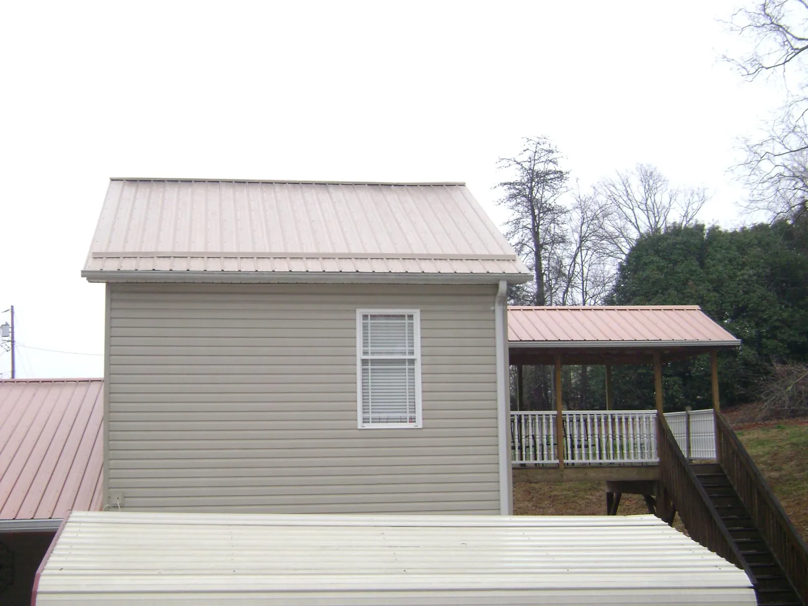 Tan metal roofs on a two story addition and attached porch, from a Roof Replacement job in Kerkhoven